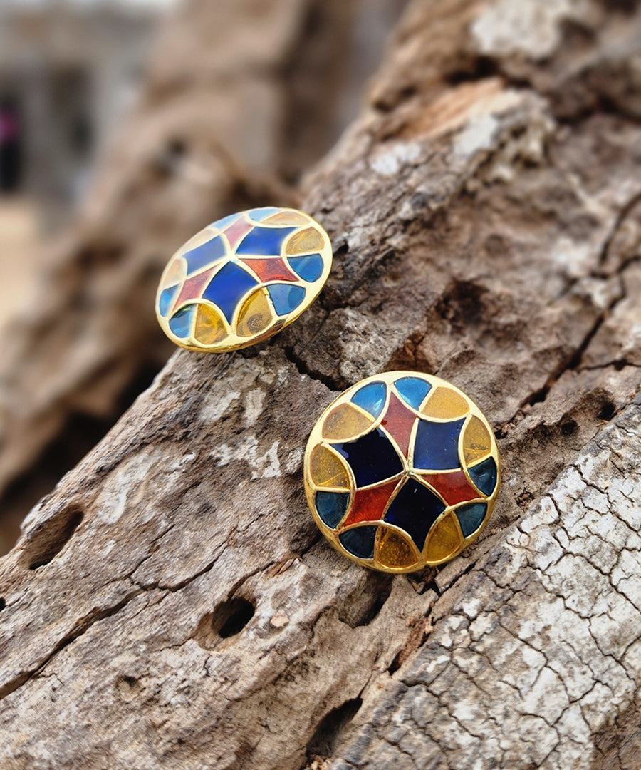 Colorful golden stud earrings lying on a wooden block. Silver earrings by Manner India.